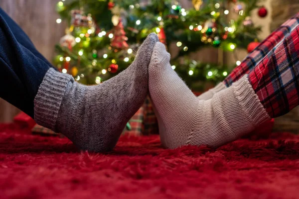 冬の靴下の男性と女性の足が互いに触れています 男と女はクリスマスツリーの近くに贈り物と座っている コンセプト — ストック写真