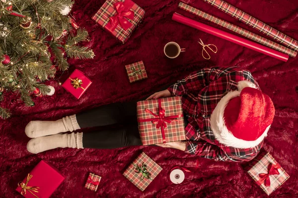 膝の上にクリスマスギフトボックスを持つ女性のトップビュー クリスマスツリーの近くで遊ぶふわふわの上に座っている家族のための女性の包装ギフト — ストック写真