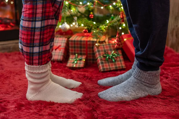 Kış çoraplarıyla ayak uçlarında duran kadın ayakları, hediyelerle dolu bir Noel ağacının yanındaki tüylü kırmızı bir battaniyenin üzerinde duruyor. Kavram 