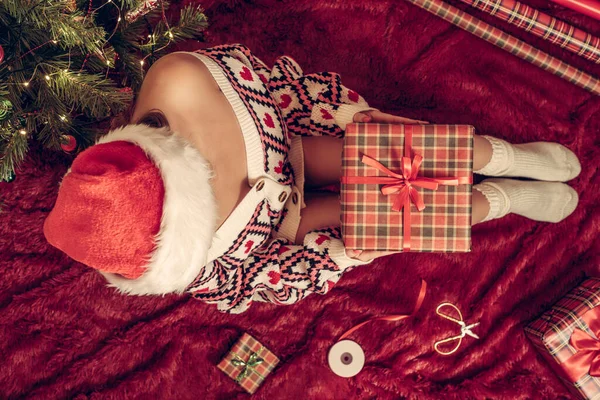 Dizlerinin üzerinde Noel hediyesi kutusu olan bir kadının en iyi görüntüsü. Noel ağacının yanındaki kabarık ekose üzerinde oturan aile için kadın paketleme hediyeleri. Düz yatıyordu.