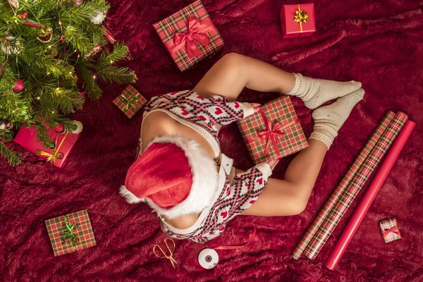 Kırmızı Noel Baba şapkalı bir kadının, Noel ağacının yanındaki kabarık ekose kumaşta oturan aile için Noel hediyesi kutularını paketlediği en iyi manzara. Düz yatıyordu.