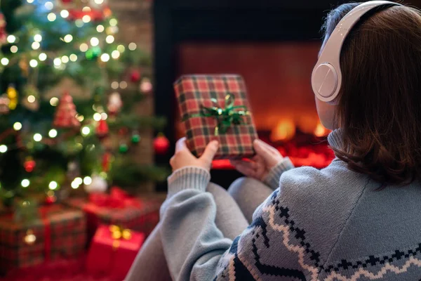 女性でヘッドフォンでクリスマスギフトボックスで手に座ってふわふわ暖炉とクリスマスツリーの近くで再生 — ストック写真