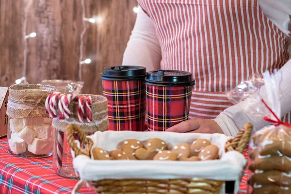 Christmas pastry shop. Woman seller, waitress selling hot chocolate in paper cup, gingerbread, marshmallows, cookies, sweets in a small cozy cafe. — Stock Image Christmas Pastry Shop Woman Seller Waitress Selling Hot Chocolate Paper Stock Photo