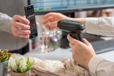 Kadın kasiyer, barkod tarayıcı kullanarak QR kodunu alıcıdan tarıyor. Erkek, kadın giyim mağazasından reklam kodu kullanarak hediye alıyor.. 