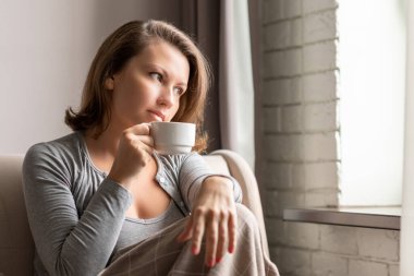 Kafkasyalı güzel bir kadının portresi kanepede battaniyeyle oturmuş, fincandan sıcak kahve içip pencereye bakıyor..