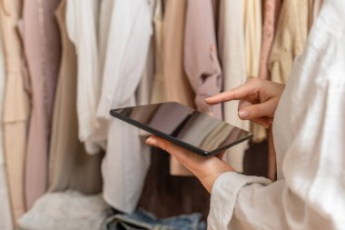 Kadın girişimci moda giyim mağazasında envanter sayımı yaparken elinde tablet tutuyordu.