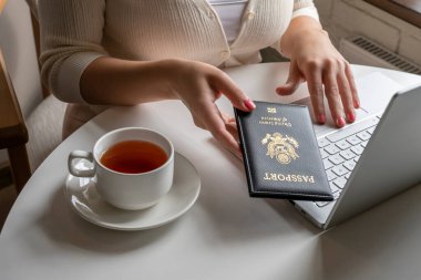 Kadın turist bir fincan kahveyle kahvaltı yapıyor. Amerikan pasaportunu havaalanındaki kafenin penceresinin yanındaki masaya koyuyor. Seyahat kavramı 
