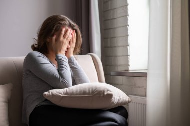 Üzgün, korkmuş, elleriyle yüzünü kapatıp ağlayan bir kadın. Yalnız kız, pencerenin yanında oturuyor, yastıkla apartman dairesinde..