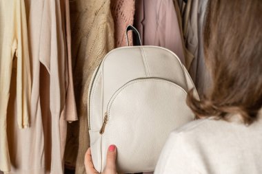 Kadın alışverişçi, müşteri küçük deri sırt çantası ve kıyafet seçiyor. Giyim mağazasında çeşitli kadın kıyafetleri. Alışveriş..
