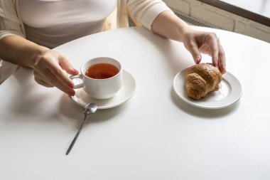 Kahvaltının tadını çıkaran bir kadın kahve ve kruvasanla kafenin penceresinin yanında oturuyor..