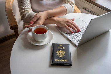 Kadın turist bir fincan kahveyle kahvaltı yapıyor. Amerikan pasaportunu havaalanındaki kafenin penceresinin yanındaki masaya koyuyor. Seyahat kavramı 