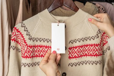 Etikete bakan kadın giysi mağazasında süveter ve Noel süsü seçiyor. Alışverişe. Kış