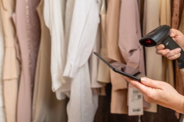 Kadın girişimci elinde tablet, barkod tarayıcısı moda giyim mağazasında envanter çıkarırken...