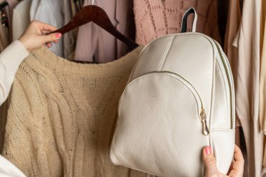 Küçük deri sırt çantası seçen bir kadın, dolaptaki giysiler. Sezon konsepti