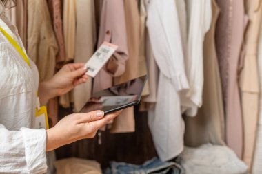 Kadın girişimci moda giyim mağazasında envanter sayımı yaparken elinde tablet tutuyordu.