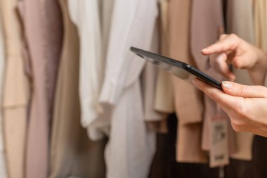Kadın girişimci moda giyim mağazasında envanter sayımı yaparken elinde tablet tutuyordu.