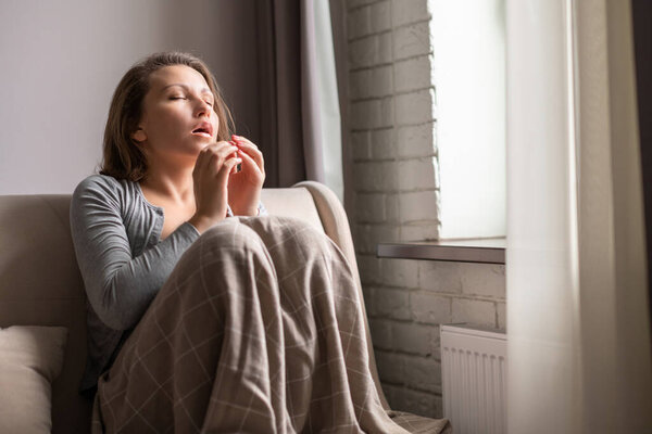 Sick brunette woman sneezing sitting on the couch in the living room near window