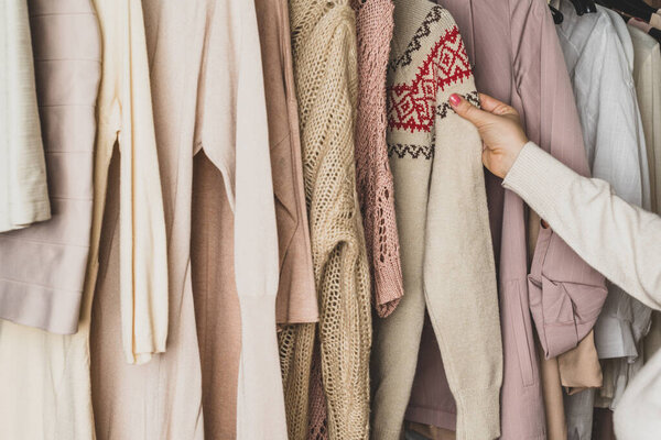 Woman shopper, customer choosing winter pulover with chtistmas ornament from assortment of clothing in garment store. Shopping. Winter