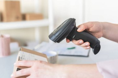 Postanenin kadın çalışanı. Müşteri gönderdiğini onaylamak için barkod tarayıcısı kullanıyor. Ev teslimat servisi.