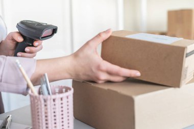 Postanenin kadın çalışanı. Müşteri gönderdiğini onaylamak için barkod tarayıcısı kullanıyor. Ev teslimat servisi.