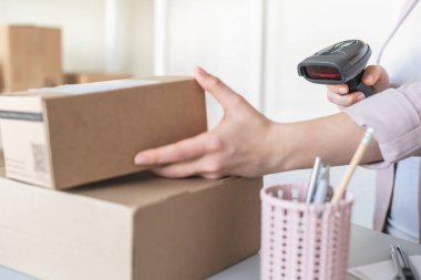 Postanenin kadın çalışanı. Müşteri gönderdiğini onaylamak için barkod tarayıcısı kullanıyor. Ev teslimat servisi.