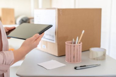 İş yerinde tabletli bir kadın, küçük bir işletme sahibi. Müşteriye teslim etmek için karton kutu ürün. e-ticaret, paketleme, çevrimiçi satış kavramı.