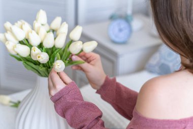 Beyaz laleleri vazoya koyan kadın oturma odasındaki kahve masasında oturuyor. Buket besteliyorum. Yaşam biçimi