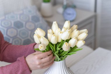 Beyaz laleleri vazoya koyan kadın oturma odasındaki kahve masasında oturuyor. Buket besteliyorum. Yaşam biçimi