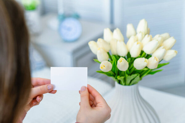 Женщина вытаскивает открытку из букета белых цветов тюльпанов. Принято. Mock up