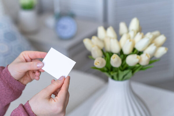 Женщина вытаскивает открытку из букета белых цветов тюльпанов. Женский день, пространство для копирования. Mock up