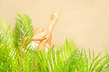 Yalnız bir kadın palmiye dallarının altında otururken tenine güneş kremi sürüyor. Yaz tatilinde kumsalda bir kadının dinlenmesi. Üst görünüm