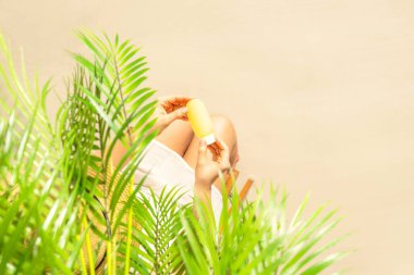 Yalnız bir kadın palmiye dallarının altında otururken tenine güneş kremi sürüyor. Yaz tatilinde kumsalda bir kadının dinlenmesi. Üst görünüm