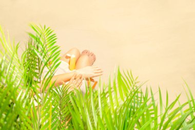 Yalnız bir kadın palmiye dallarının altında otururken tenine güneş kremi sürüyor. Yaz tatilinde kumsalda bir kadının dinlenmesi. Üst görünüm