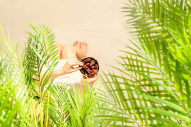 Hasır şapkalı bir kadın hindistan cevizi palmiyesi dallarının altında oturmuş elinde kraliyet meyveleri kumsaldaki bir kasede tutuyordu. Yaz. Üst görünüm