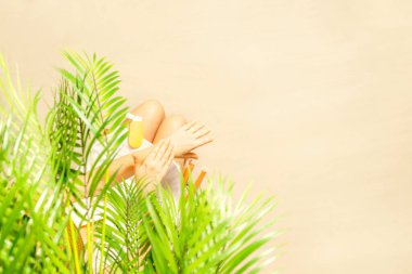 Yalnız bir kadın palmiye dallarının altında otururken tenine güneş kremi sürüyor. Yaz tatilinde kumsalda bir kadının dinlenmesi. Üst görünüm
