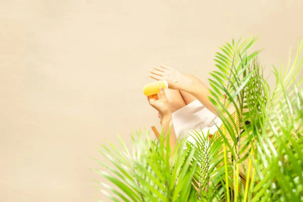 Alone woman applying sunscreen on skin sitting under palm tree branches. Female relaxation on the sand of the beach at summer vacation. Top view