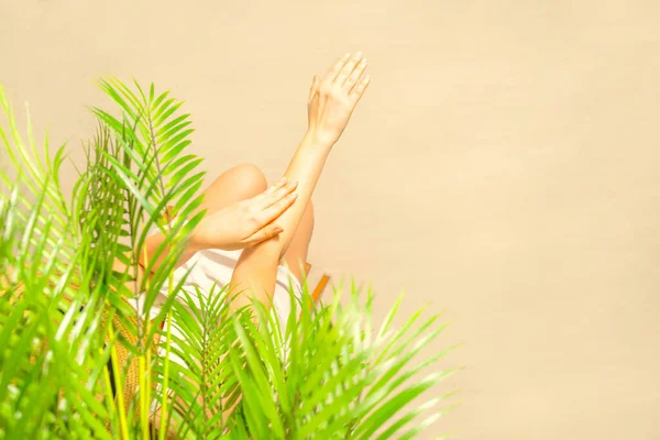 Alone woman applying sunscreen on skin sitting under palm tree branches. Female relaxation on the sand of the beach at summer vacation. Top view