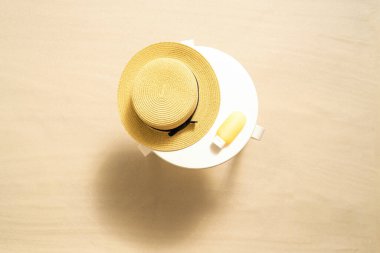 Kumlu kumsaldaki beyaz masada korunmak için güneş kremi ve hasır şapka. Yaz tatili. Üst görünüm