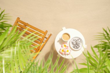 Kumlu sahilde palmiye ağaçlarının altında, üzerinde çikolatalı kurabiyeler olan bir fincan kahve. Açık hava kafesi. Üst görünüm