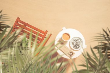 Kumlu sahilde palmiye ağaçlarının altında, üzerinde çikolatalı kurabiyeler olan bir fincan kahve. Açık hava kafesi. Üst görünüm