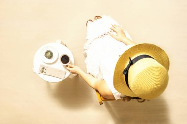 Plajda sıcak kahve ve çikolatalı kurabiye içen bir kadın masada oturup egzotik yaz tatilinin tadını çıkarıyor. Açık hava kafesi. Üst görünüm