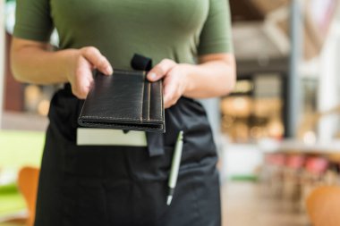 Önlüklü kadın garsonun kesilmiş görüntüsü kafe ya da restoran ziyaretçisine fatura klasörünü uzat.
