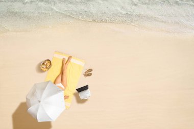 Dizüstü bilgisayarı, çantası, kulaklığı olan bir kadın şemsiyesi altında deniz kıyısındaki havlunun yanında oturuyor. Yaz tatili. Hava görünümü