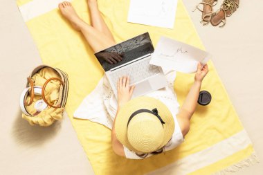 İş kadını serbest çalışan, kumsal havlusunda oturup kahve içen ve grafikler ve grafiklerle dizüstü bilgisayarda çalışan biri. Yaz tatili. Hava görünümü