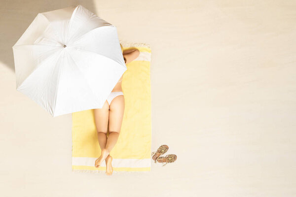 Одна женщина в бикини сидит и загорает на желтом пляжном полотенце. под зонтиком. Женский отдых на песчаном пляже во время летних каникул. сверху, вид с воздуха