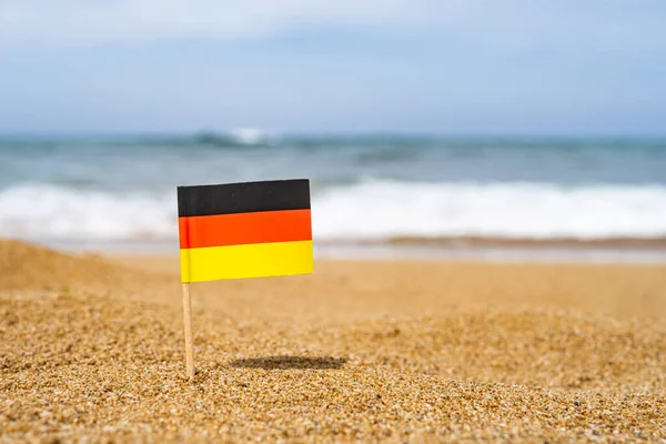 해변의 파도가 밀려오는 속에서 이쑤시개 모양의 독일의 깃발이었습니다 — 스톡 사진