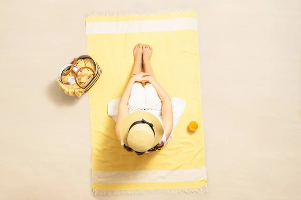 Alone sad woman in straw hat and dress hugging her legs sitting on yellow beach towel. Aerial view