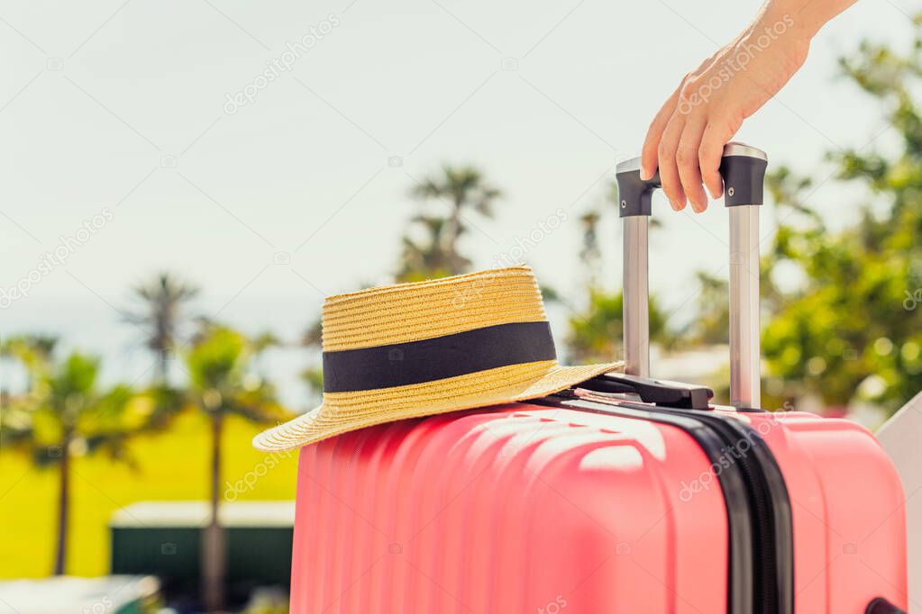 Woman with pink suitcase and beach hat standing on passengers ladder and getting out of airplane opposite sea coastline with palm trees. Tourism concept