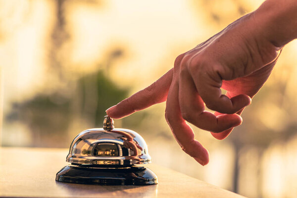 Woman cook, waitress of beach restaurant ringing service bell to warn that the dish is ready. Roof of cafe sea and palm tree view on sunset. 
