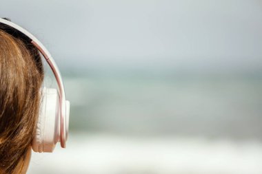 Sahilde tek başına oturan, kulaklıklarıyla müzik dinleyen, hayal kuran ve denize bakan bir kadın. Yaz tatilinde kadın dinlenmesi.